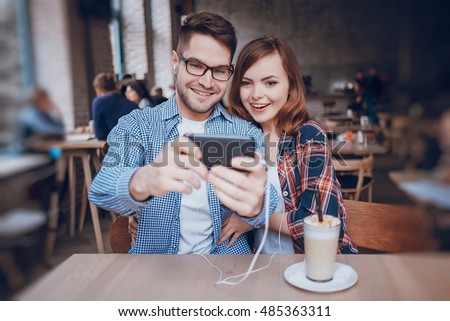 The boy and girl resting in cafe, photographed on the phone and listening to music on headphones