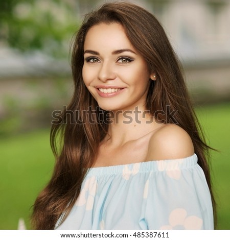 Young beautiful woman with long brunette hair and perfect smile. Happy girl posing in park and looking in camera