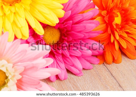 Colorful fabric daisies on wooden background, closeup picture.