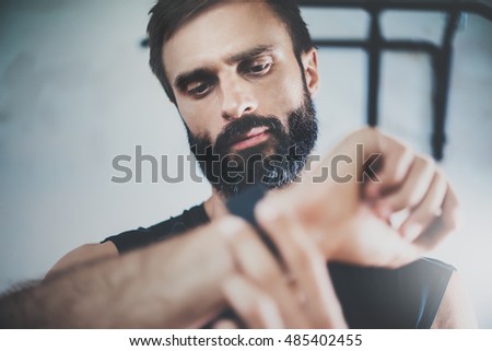 Portrait Bearded Sportive Man After Workout Session Checks Fitness Results Smart Watch.Adult Guy Wears Sport Tracker Wristband Arm.Training hard inside gym.Horizontal bar background.Blurred