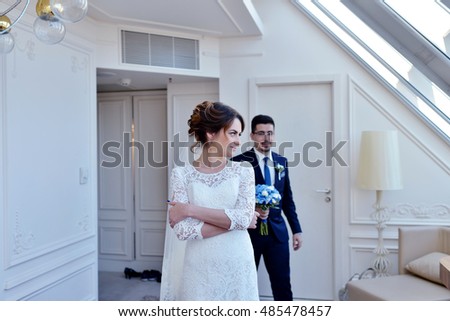 Handsome groom is seeing first the beauty bride in the morning. Meeting of a wedding couple. Beautiful model girl in white dress and in lace veil. Man in suit. Female and male portrait. Woman and guy
