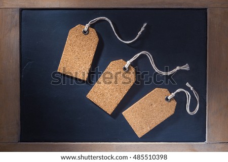 Empty cork tags on small chalkboard with wooden frame, hard lighting with hard shadows
