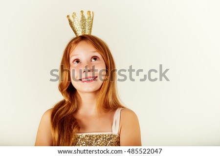 Pretty little girl with beautiful red hair looking up. Little princess with a crown on her head. Kids fashion. toned image