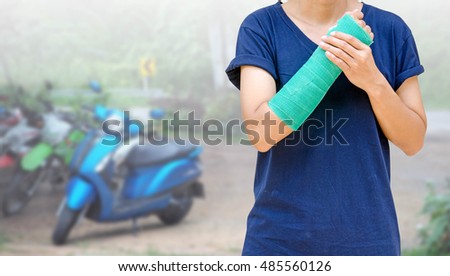 arm broken with green cast on blurred motorcycle background, accident insurance concept.