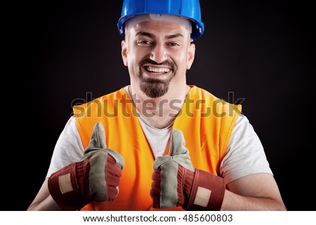 Happy construction worker with full protective gear making thumbs up sign- hardhat, protective gloves and orange reflective vest. Concept image.