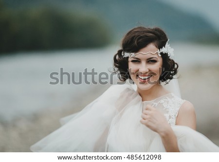 Gorgeous bride with short brunette hair smiles while posing by the river Royalty-Free Stock Photo #485612098