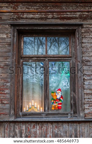 Old wooden window in dwelling decorated with candles, Santa and deer pictures. Meeting holiday.