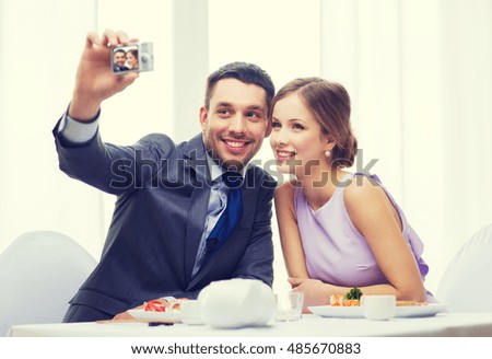restaurant, couple, technology and holiday concept - smiling couple taking self portrait picture with digital camera at resaturant