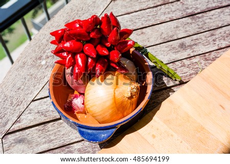 Cooking: onion, garlic and chilli pepper in a dish on top of a wooden table