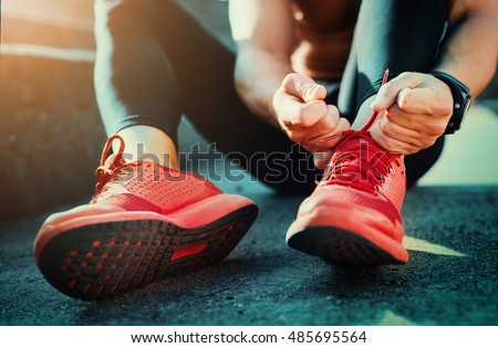 Man tying jogging shoes.He is running outdoors on a sunny day. Royalty-Free Stock Photo #485695564