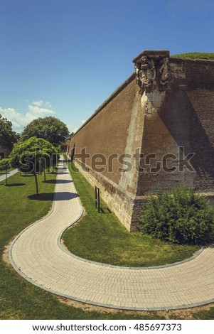 Historical site of the spectacular White Carolina medieval fortress with weathered fortification brick walls, green lawns, ornamental trees and paved alleys in Alba Iulia, Romania.
