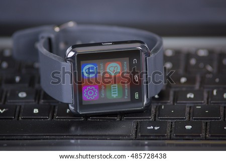 Smartwatch with screen lit up sitting on top of computer keyboard, very nice all black concept