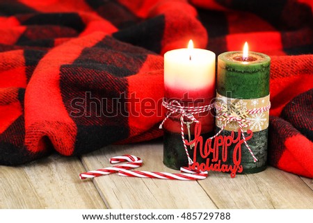 Christmas candles, Happy Holidays, and candy canes by red and black checkered wool blanket on antique rustic wood background