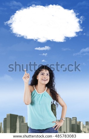 Cheerful Indian woman thinking idea while looking up and pointing at cloud
