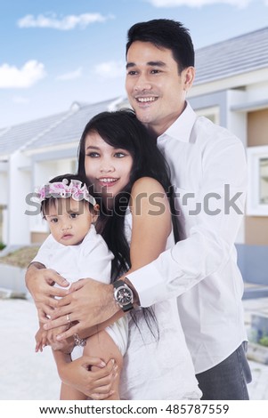 Image of happy Asian parents and their daughter standing at new residential
