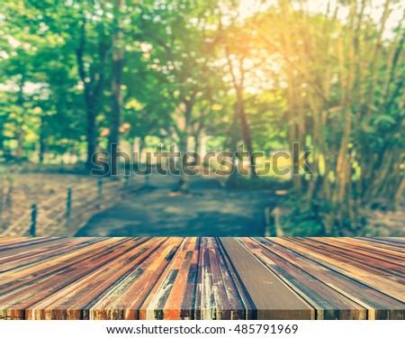 wood table and vintage tone blur image of walk way or road in green garden for background usage .