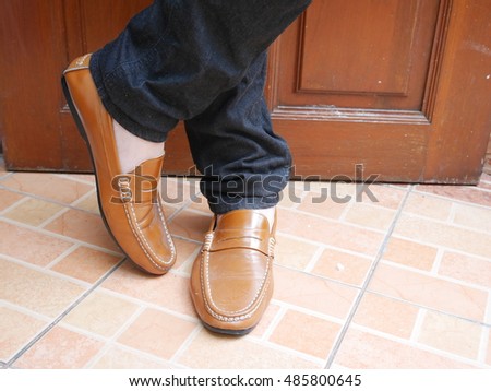 Young fashion man's legs in blue jeans and brown boots on wooden floor