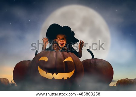 Happy Halloween! Cute little witch with a big pumpkin. Beautiful young child girl in witch costume outdoors. 