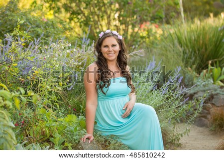 Young pregnant woman relaxing in park outdoors, healthy pregnancy. Beautiful pregnant woman holding her tummy. Pregnant woman walking in park