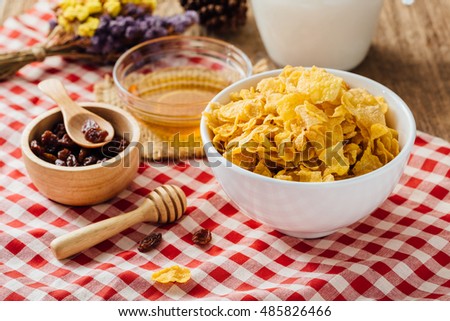 corn flakes with honey, currant and milk on red table cloth