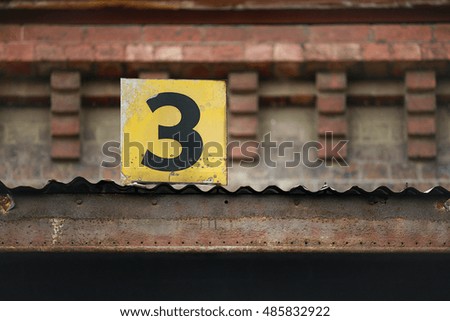 The number three painted on a small metal sign and mounted on building
