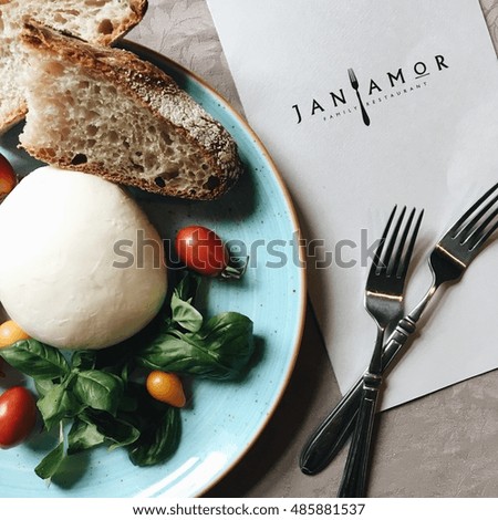 Fresh vegetables and cheese on a plate with forks and menu on the restaurant table