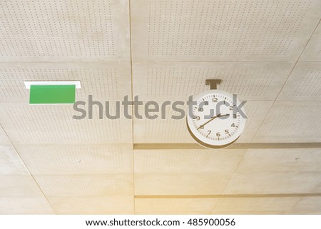 Modern circle clock and blank sign hang on ceiling under office building
