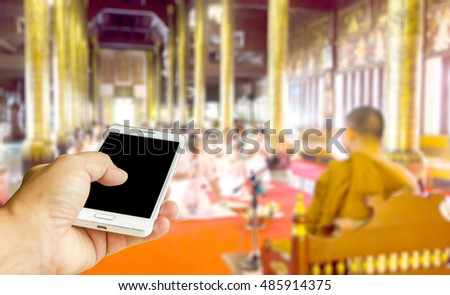 Man use mobile phone, blur image of monk preaching in temple as background.