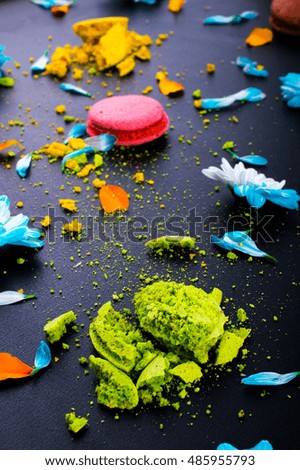 Crushed green, pink, yellow macaroon. Blue flowers and blue and orange petals. On a black background. Macro. Close up