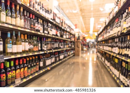 Blurred image of wine shelves display in supermarket. Defocused  Rows of Wine Liquor bottles on the store shelf. Alcoholic beverage abstract background. Alcohol drink market concept.