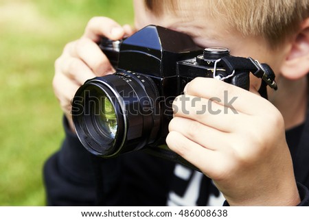 Child blond boy with vintage photo film camera photographing outside