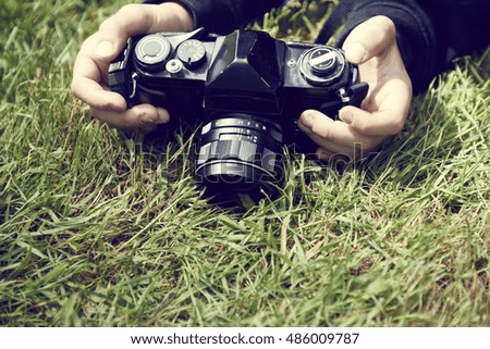 Hands holding camera on grass. Child blond boy with vintage photo film camera photographing outside