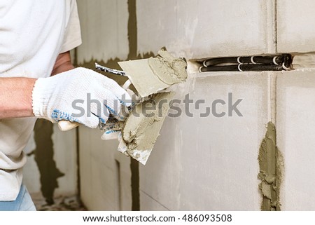 Man repairs wall with spackling paste, Construction industry worker using a putty knife and leveling concrete on concrete pillars, Worker spreading plaster to wall, corner protecting batten install