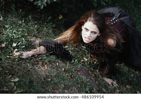 Halloween Witch  in a dark forest. Beautiful young woman in witches  costume . Halloween art design.  Horror Background For Halloween Concept