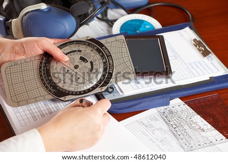 Pilot equipment with airplane pilot hand filling in flight plan, other tools like flight computer used for aviation calculations, protractor, kneepad with charts and professional headset