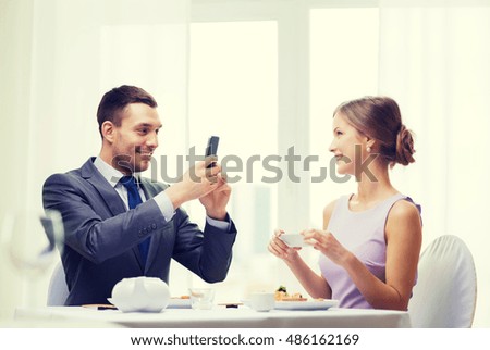 restaurant, couple, technology and holiday concept - smiling man taking picture of wife or girlfriend while picturing sushi with smartphone