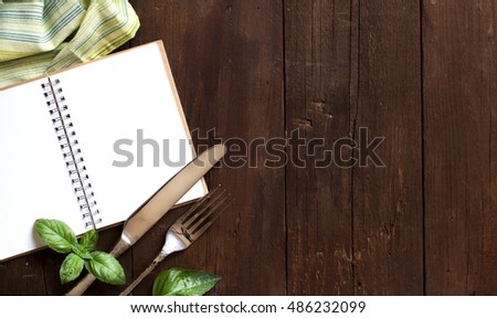 Blank cooking recipe book with fork, knife, basil and napkin on a wooden table