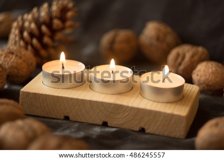 Close up of wooden candle holder made from soft wood with three tea candles and surrounded by autumn fruits.
