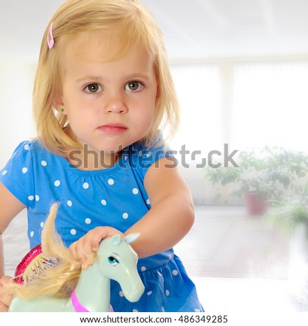 Cute little blonde girl playing with a toy horse. Girl wearing a blue dress with polka dots.Against the background of a child's room . The concept of the holiday and the New year.