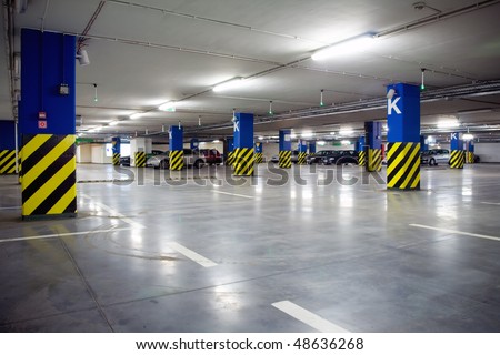 Parking garage, underground interior with a few parked cars. Neon light in bright industrial building.