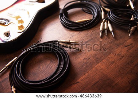 Setting up an recording environment in a studio. Professional instrument cables coiled on a studio floor. An electric guitar in background. Intentionally shot in low key tone. Soft focus.