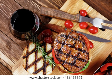 fresh grilled beef double huge hamburger served on wooden plate with wine cherry tomatoes and rosemary over table