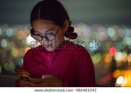 Young Asian woman using smartphone on background building bokeh at night time in Osaka , Japan.