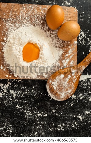 Two chicken eggs with wheat flour and yolk on board with wooden spoon on blackboard kitchen table. Homemade baking concept with space. Template for bakery book cover