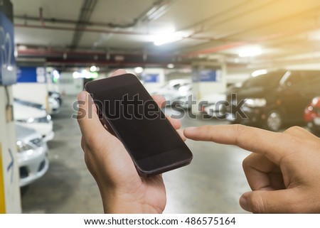 Hand of a man holding a smartphone and touching the screen.Parking lot