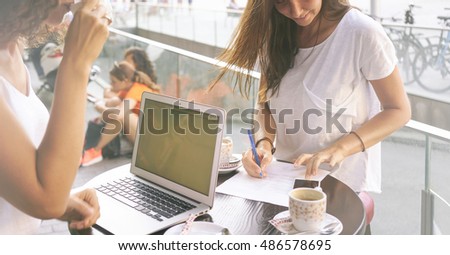 A cropped photo of two females working outdoors by using a portable computer. Two female bloggers are working on the new article while sitting with a laptop in a street cafe.