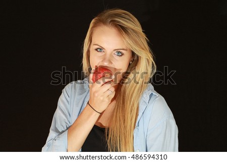 A beautiful blonde woman enjoys a red apple.