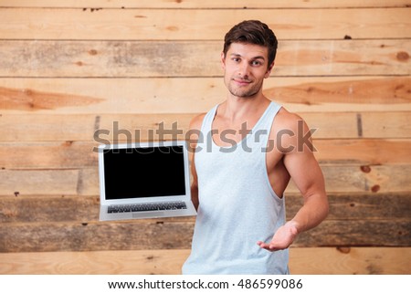 Happy young casual man holding blank screen laptop isolated on a wooden background