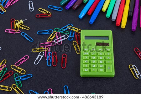 calculator, paper clips, markers on black Board. School and business concept