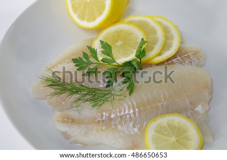 fresh raw cod fish fillet on a plate with parsley and lemon 
